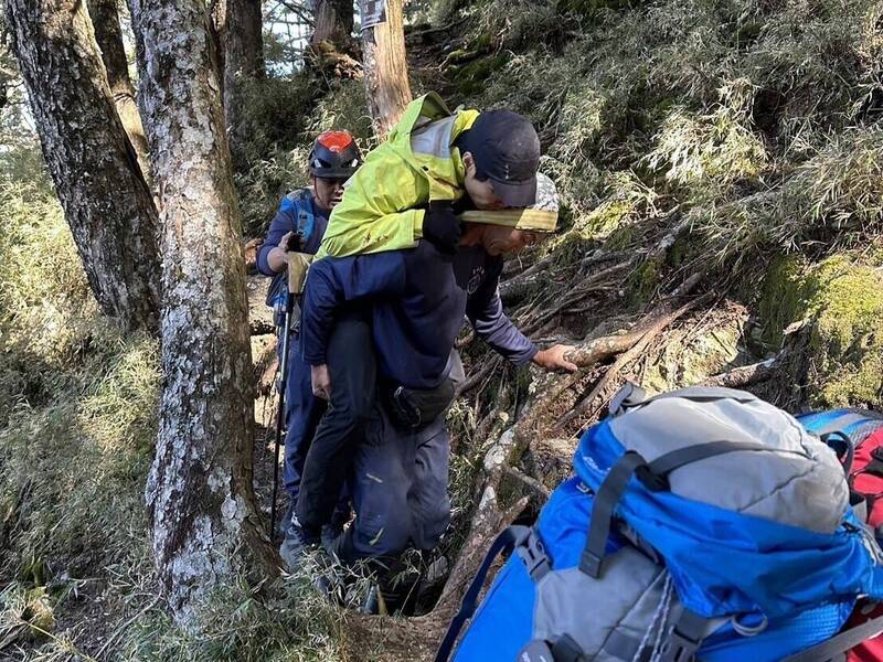 山友（绿衣）独攀单攻八通关山不慎摔到头破骨折，搜救人员以背负方式将人移至直升机起降点吊挂。（图由南投县消防局提供）